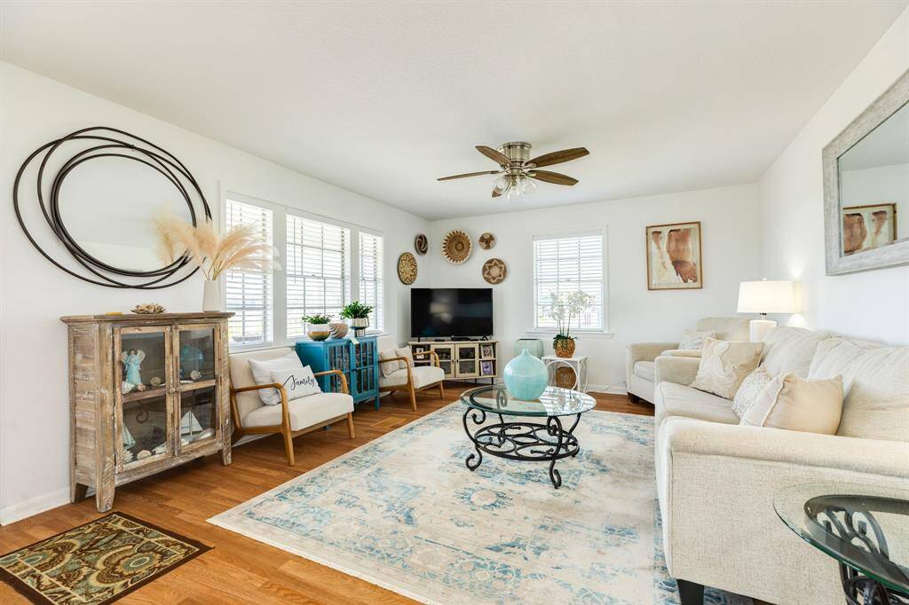 This wide-angle view showcases the bright, open living space with large windows, eclectic furnishings, and tasteful beach-themed accents that add warmth and personality.