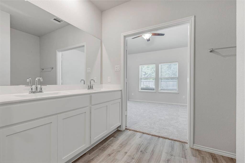 This photo showcases a modern bathroom featuring a double vanity with sleek fixtures. It opens into a bright bedroom with carpeted flooring and large windows, allowing natural light to fill the space.