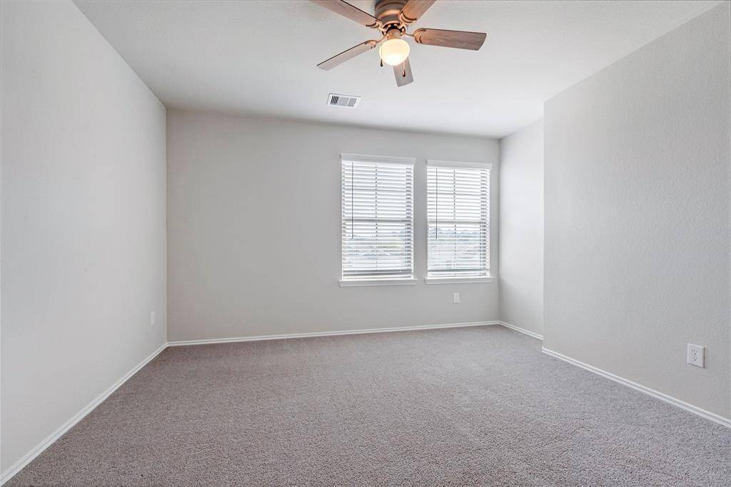 Bright and spacious bedroom with neutral walls, carpeted flooring, a ceiling fan, and two large windows for natural light.