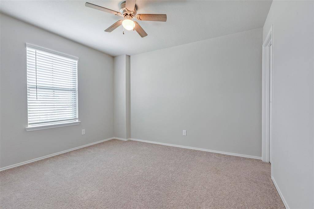 This room features neutral walls, a ceiling fan, carpeted flooring, and a window with blinds, providing a cozy and versatile space.