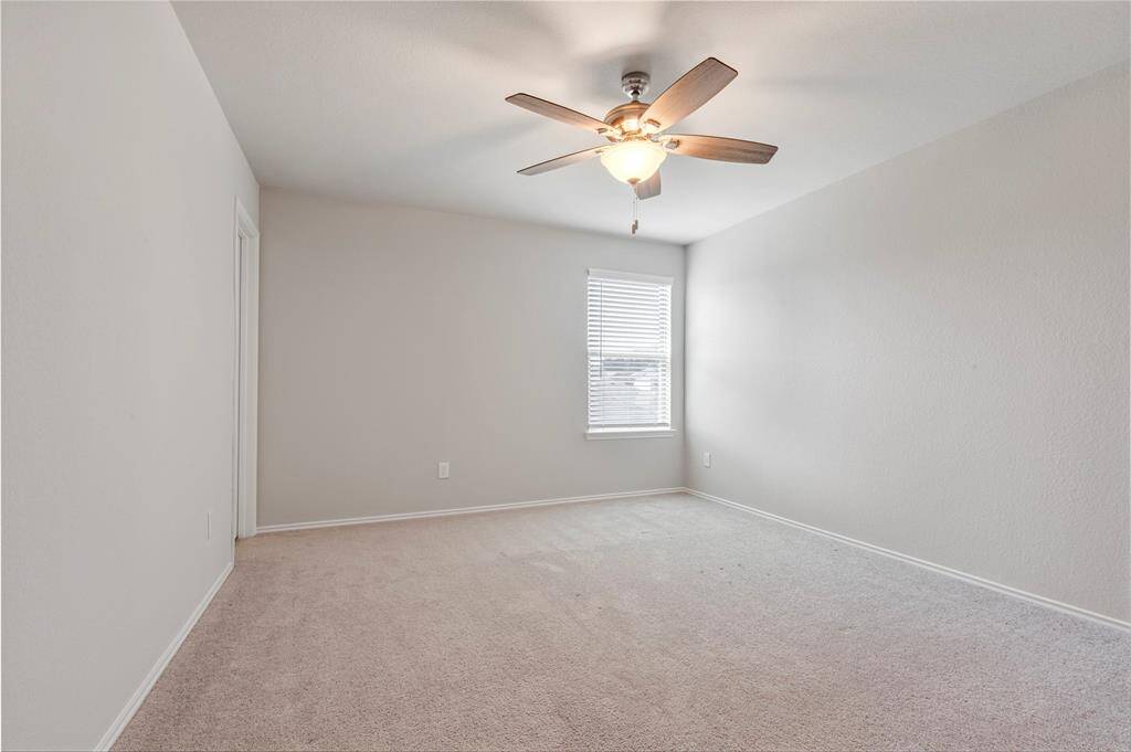 This photo shows a bright, empty room with neutral-colored walls and carpet. It features a ceiling fan with a light and a window allowing natural light to enter, creating a cozy atmosphere. Ideal for a bedroom or office space.