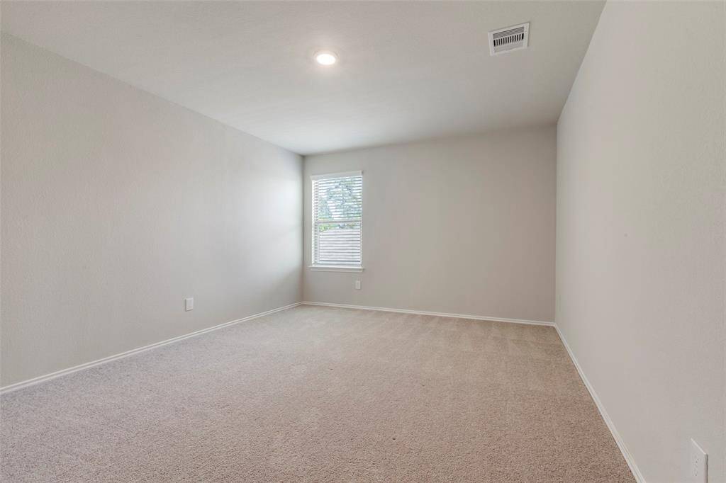 This photo shows a spacious, carpeted room with neutral walls, a window providing natural light, and a ceiling light fixture. Ideal for a bedroom or office space.