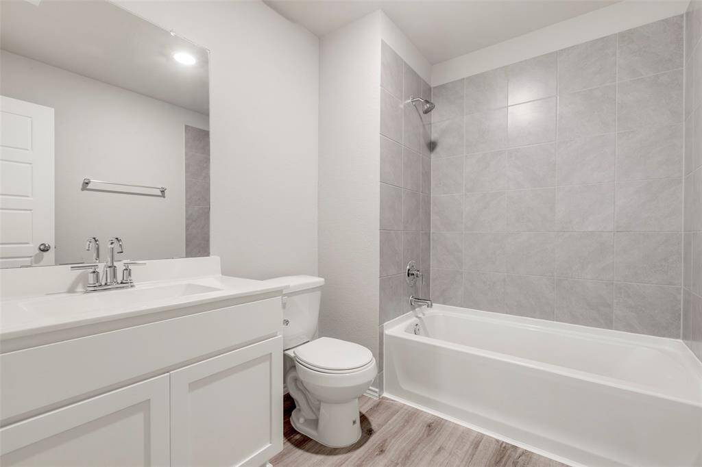 This modern bathroom features a sleek white vanity with chrome fixtures, a large mirror, and a bathtub with gray tile surround. The space is bright and airy, offering a clean and contemporary look.