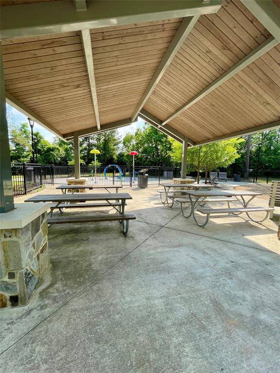 This photo showcases a covered outdoor pavilion with picnic tables on a concrete surface, ideal for gatherings. It overlooks a fenced area with a splash pad, surrounded by trees, providing a perfect family-friendly setting.