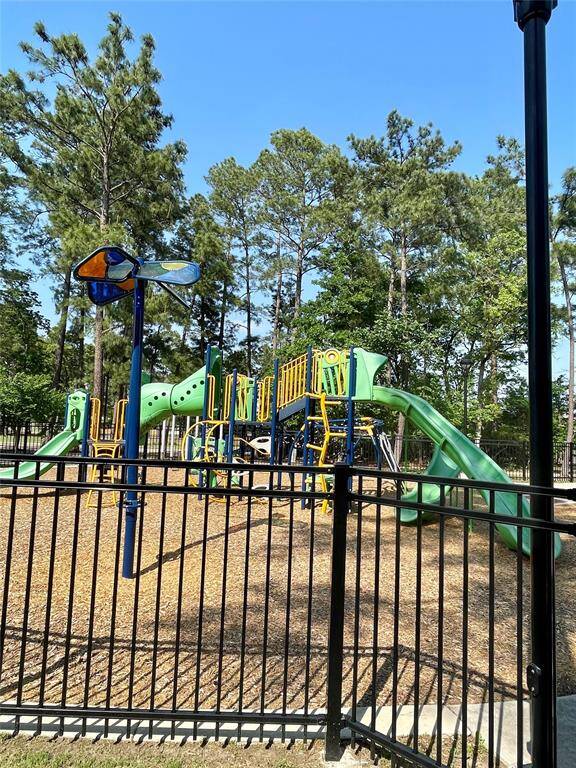 This photo shows a well-maintained playground with slides and climbing structures, surrounded by a black fence and set against a backdrop of tall trees, perfect for family-friendly living.