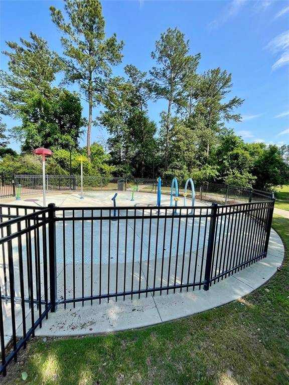 A fenced outdoor splash pad surrounded by tall trees offers a refreshing recreational space, perfect for families and children.