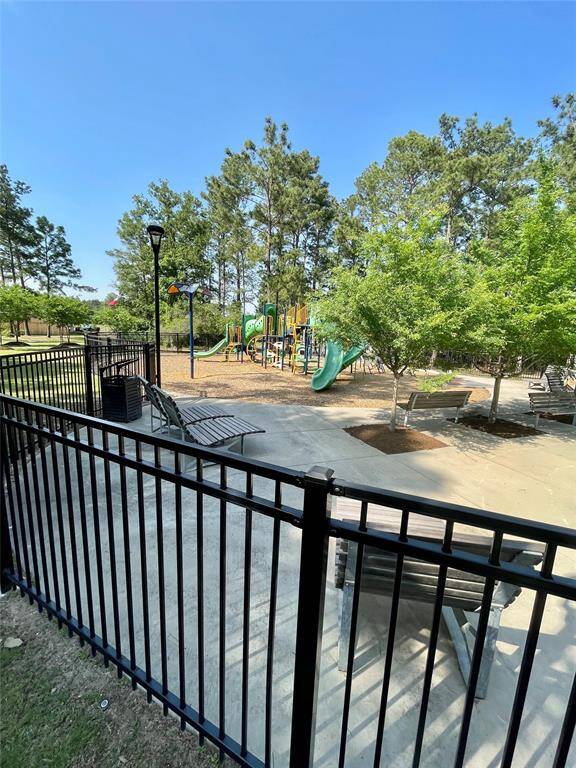 This photo shows a fenced playground area with a slide, surrounded by trees. There are benches and a pathway, ideal for families.