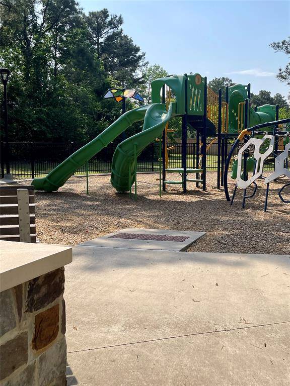 This photo shows a playground with a green slide and climbing structures, surrounded by trees and a fence, offering a family-friendly outdoor space.