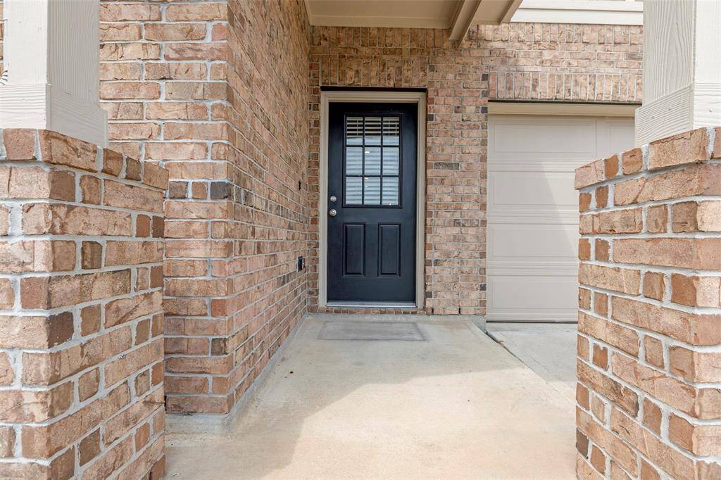 This photo showcases a welcoming brick entryway with a black front door and adjacent garage. It has a covered porch area with sturdy brick pillars, offering a charming and secure entrance to the home.