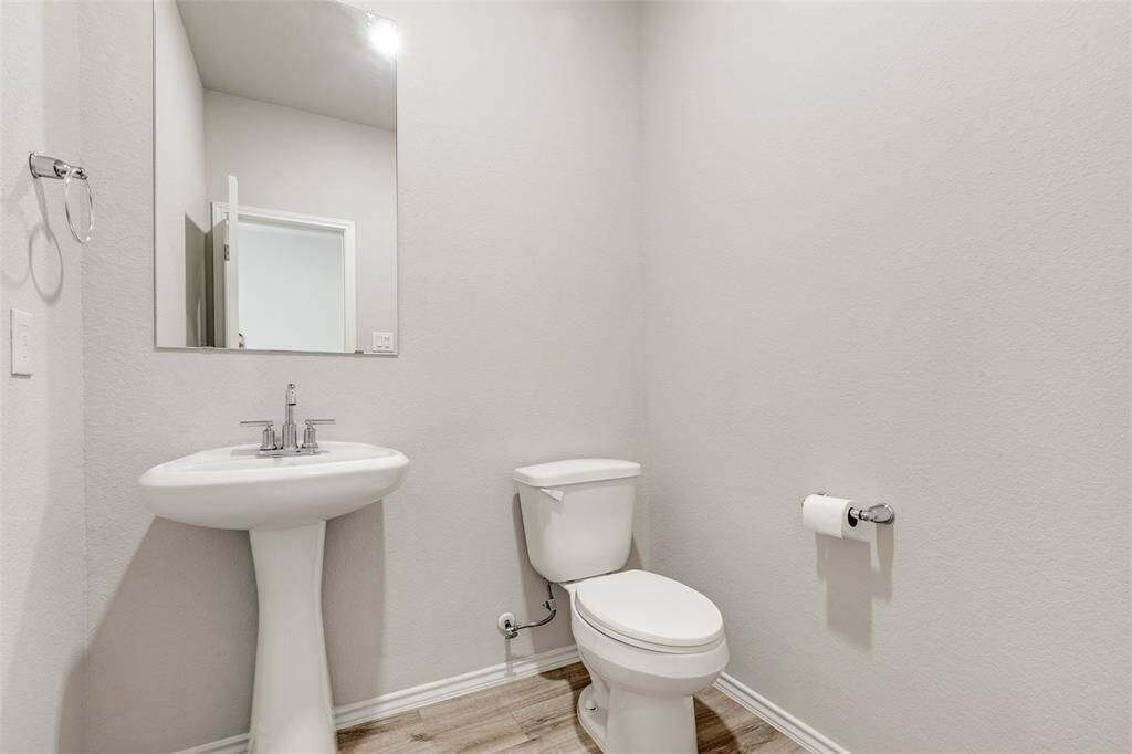This is a simple, modern half-bathroom featuring a pedestal sink, a toilet, and a large mirror, set against neutral walls with wood-style flooring.