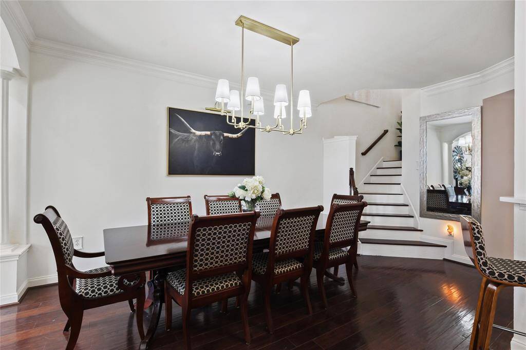 Elegant dining room with dark wood flooring and a staircase. Features a large dining table with upholstered chairs, modern chandelier, and stylish artwork. Bright, open space perfect for entertaining.