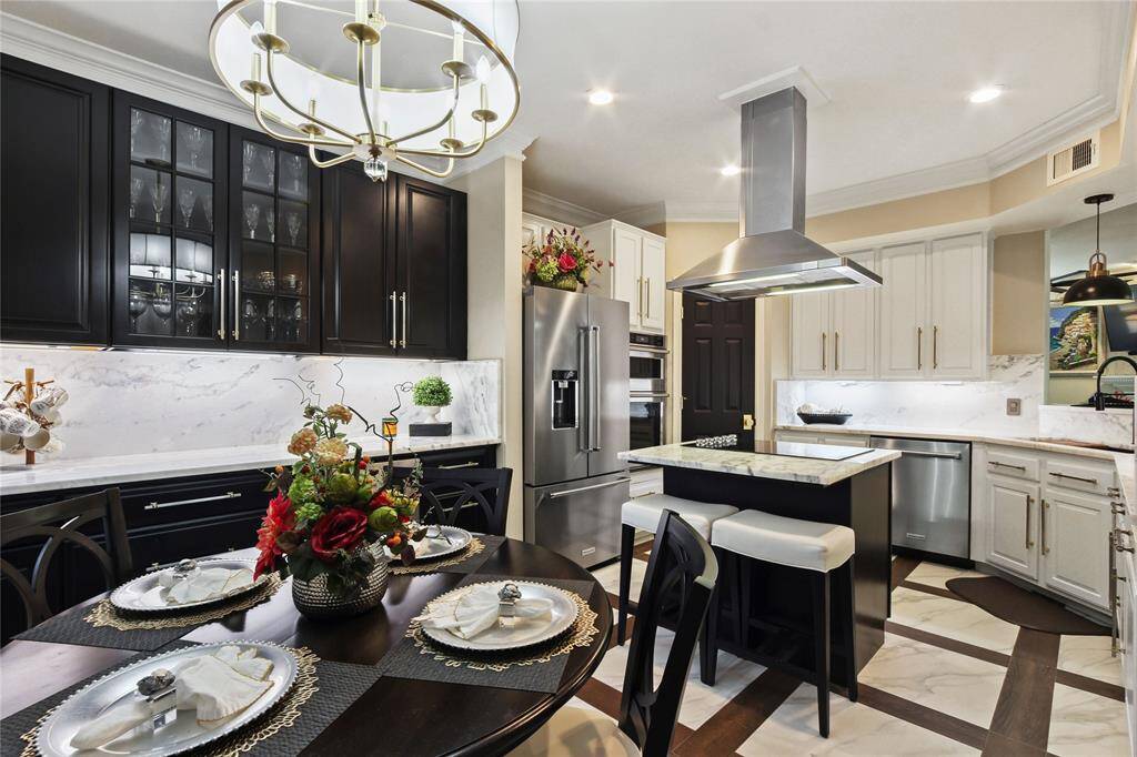 This modern kitchen features sleek dark wood and white cabinetry, stainless steel appliances, and a central island with seating. The dining area is elegantly set, and the room is illuminated by a stylish chandelier, creating a warm and inviting atmosphere.