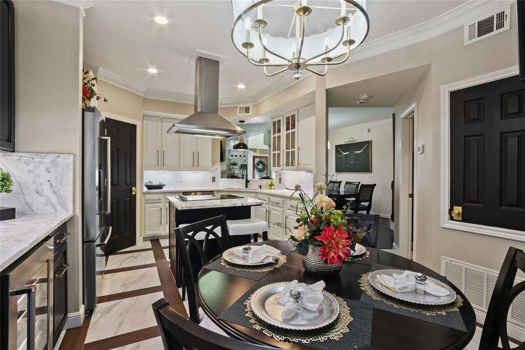 This elegant kitchen features a modern design with white and dark wood cabinetry, Quartz countertops, and stainless steel appliances. A central island with a range hood offers additional workspace. The dining area is accented by a stylish chandelier, and the overall space is open and inviting.