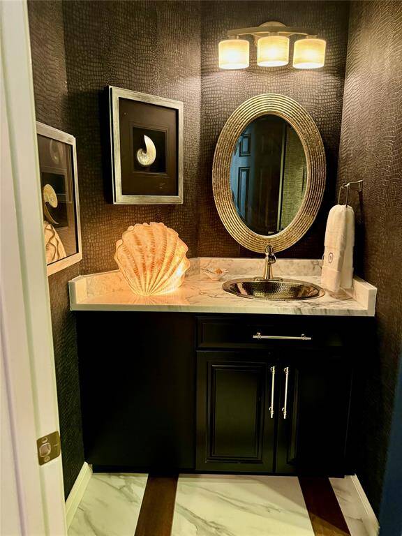 This photo shows a stylish powder room with dark textured walls and a modern vanity. It features a marble countertop, an oval mirror, and a chic light fixture. Decorative elements include framed art and a shell-shaped lamp, creating a sophisticated, coastal ambiance.