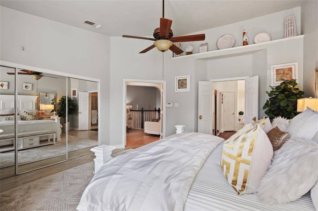 This spacious bedroom features a cozy ambiance with soft, neutral colors and elegant decor. It includes a large mirrored closet, a ceiling fan for comfort, and ample natural light. The room connects to another area, offering a seamless flow within the home.