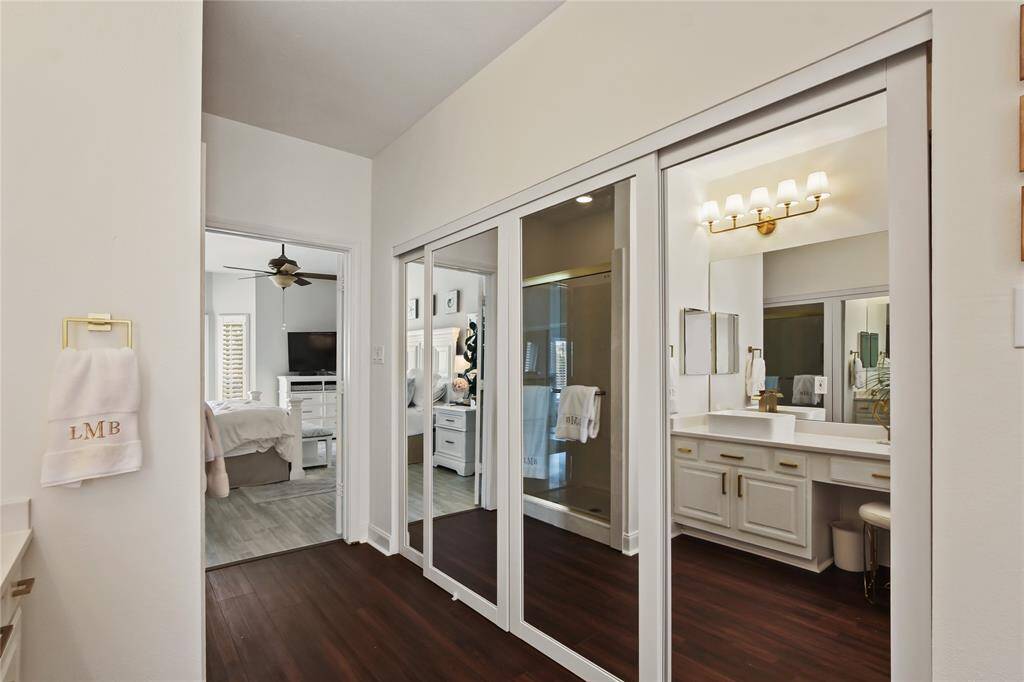 This photo showcases a bright and modern bathroom with a double vanity, large mirrors, and elegant lighting. The space leads into a bedroom featuring a ceiling fan and light-colored flooring, creating a cohesive and stylish look.