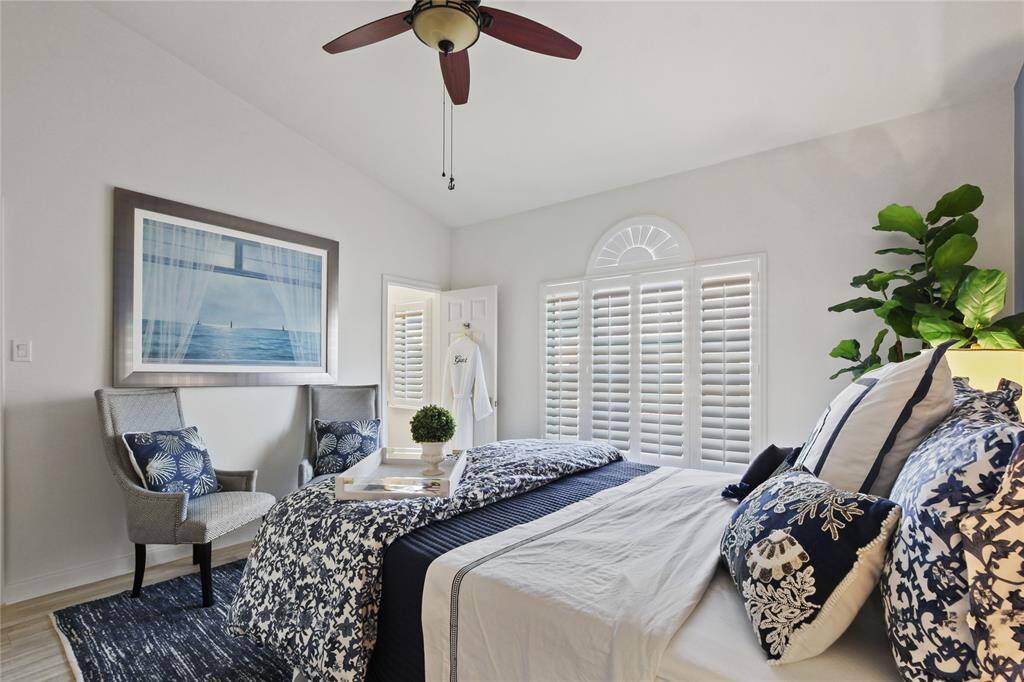 Bright and airy bedroom with stylish decor, featuring a ceiling fan, large windows with shutters, and comfortable seating. The serene atmosphere is complemented by tasteful artwork and lush greenery, making it a perfect retreat.