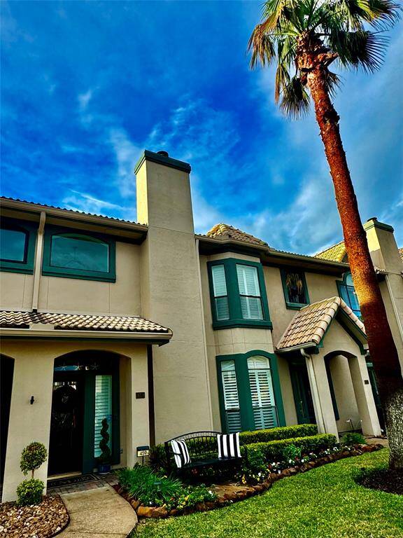 This photo showcases a two-story home with a modern Mediterranean design, featuring a tiled roof and a well-maintained front yard. A tall palm tree stands prominently, and large windows with shutters add elegance to the facade. Enter your front door ground level no stairs.
