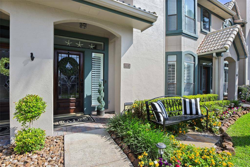 Charming home entrance with a welcoming front porch, featuring a decorative wreath on a wooden door, neatly landscaped garden, and a cozy bench. Ground level no stairs.