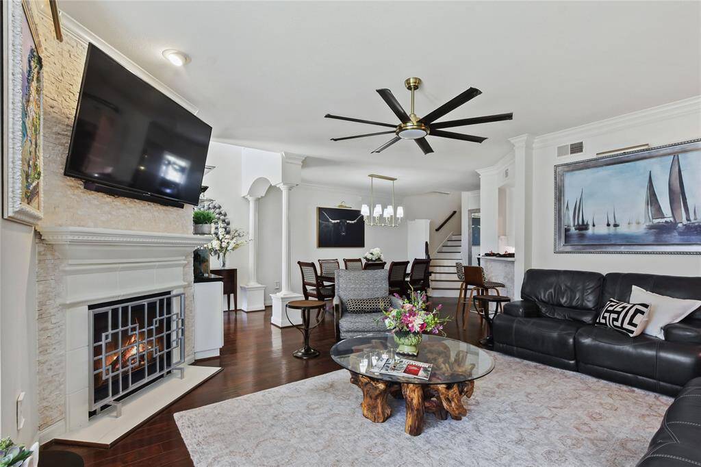 This spacious living room features a cozy fireplace, mounted TV, and elegant wood flooring. The open layout includes a stylish dining area with modern lighting, and the room is tastefully decorated with a large sectional sofa and unique coffee table. Perfect for entertaining and relaxation.  Light and Bright.