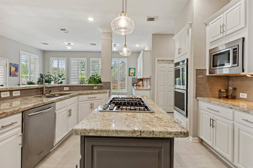 Updated kitchen with white cabinetry and dark taupe island with gas cooktop. Stainless steel appliances include double ovens, built-in microwave, dishwasher and double basin sink.