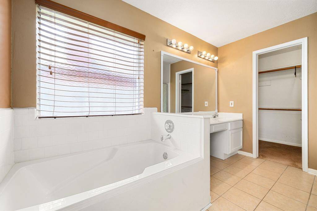 This primary bathroom is definitely move-in ready! Featuring a separate garden tub for soaking after a long day with custom tile detailing, light stained cabinets with light countertops, spacious walk-in closet with shelving, high ceilings, custom paint, sleek finishes.
