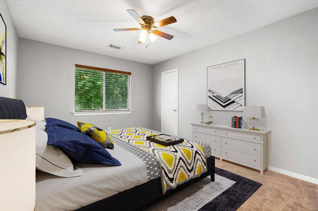 Secondary bedroom features plush carpet, custom paint, dark stained ceiling fan with lighting and a large window with privacy blinds. *Virtually Staged