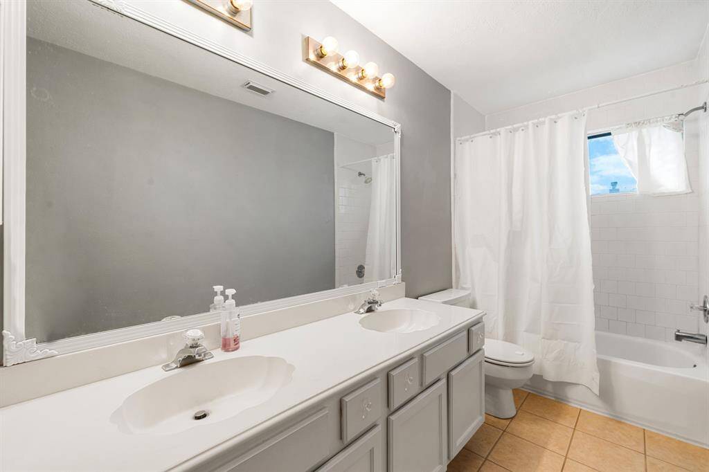Secondary bathroom features light countertops and cabinets, custom paint, shower/tub combo with tile surround, large mirror, tile floors, sleek fixtures and modern finishes, plenty of space to accommodate any visiting family or guests.