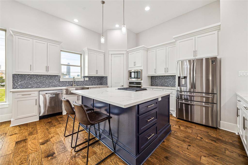 The spacious kitchen features a central island with ample storage and a built-in cooktop, perfect for meal preparation and entertaining. Stainless steel appliances add a sleek, modern touch, while providing both style and functionality for the home chef.
