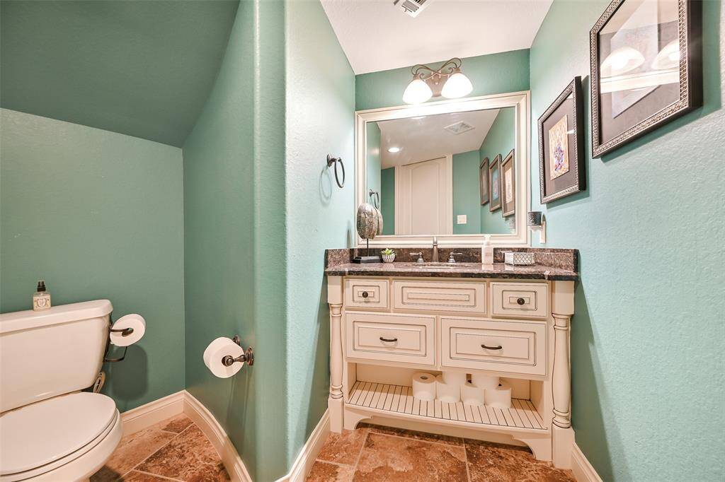 This bathroom features a stylish vanity with a granite countertop and ample storage. The walls are painted a soothing blue, complementing the warm tile flooring.