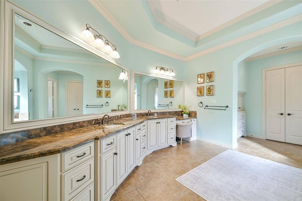 This bathroom features elegant countertops, dual sinks, and custom cabinetry. The space includes a makeup vanity area creating a luxurious and inviting atmosphere.