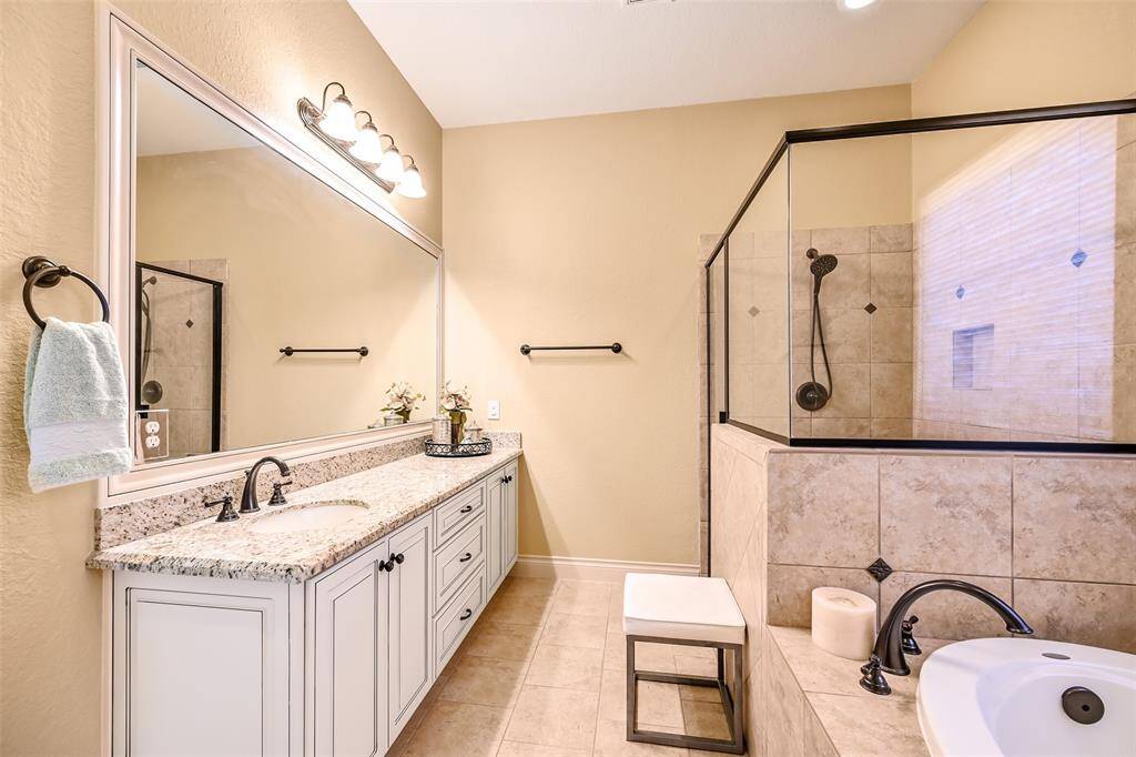 This bathroom features a spacious layout with a large granite countertop, large vanity, and ample lighting. It includes a glass-enclosed shower with decorative tiles and a separate bathtub, creating a luxurious and functional space.