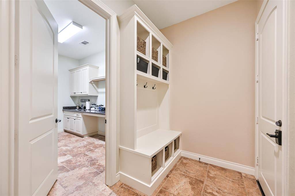 This photo showcases a mudroom with built-in storage and bench seating, leading to a bright laundry room with cabinets and counter space. The tile flooring is consistent throughout, creating a cohesive look.