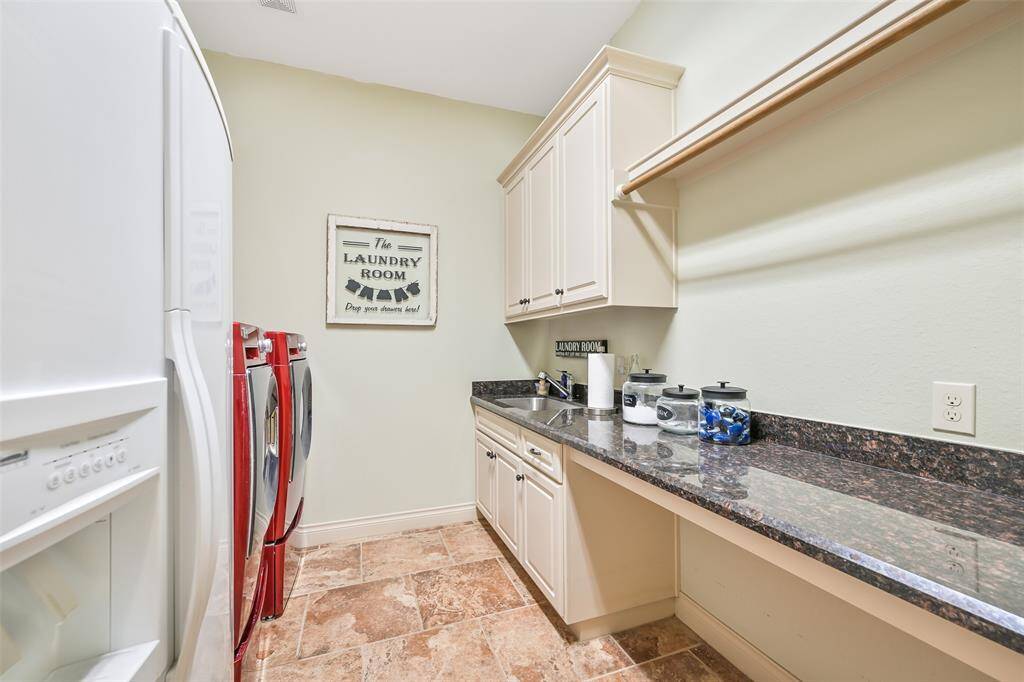 This photo showcases a well-organized laundry room featuring ample countertop space, overhead cabinets for storage, and a convenient utility sink. The room is bright and functional, with space for a second refridgerator.