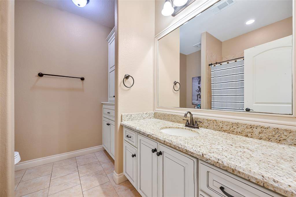 This bathroom features a spacious granite countertop with an under-mount sink, ample cabinetry for storage, and a built in laundry hamper.