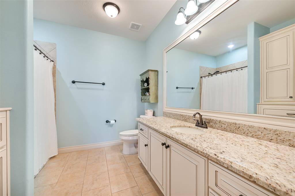 This bathroom features a spacious layout with light blue walls, a large granite countertop with ample cabinetry with built in laundry hamper and a shower-tub combo.