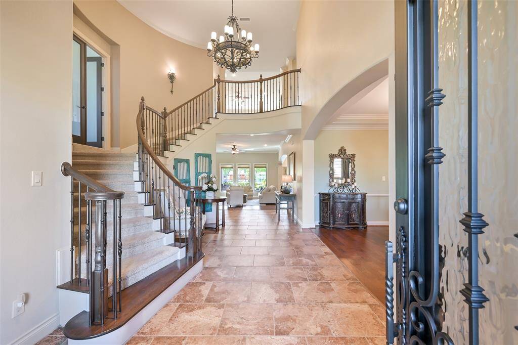 This elegant foyer features a grand curved staircase with wrought iron railings, a landing for the study entrance, high ceilings, and a mix of tile and wood flooring. It opens into a spacious living area with natural light and stylish decor, creating a warm and luxurious entrance.
