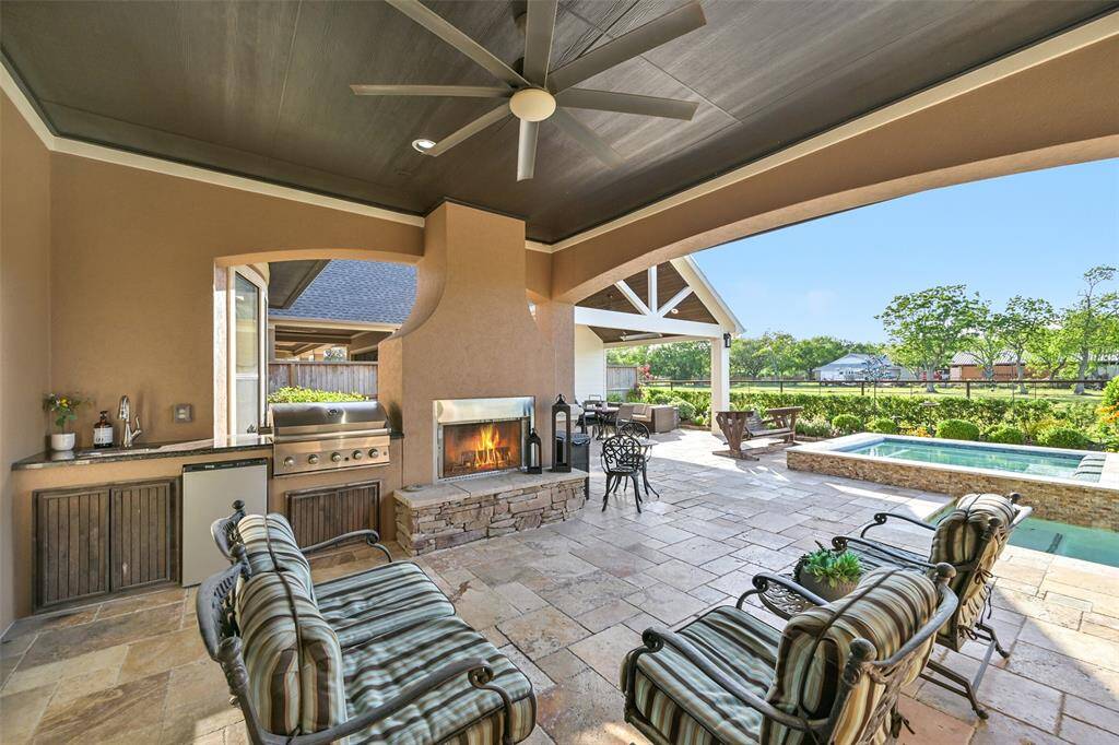 This outdoor space features a covered patio with a built-in grill, stucco and stone fireplace, and comfortable seating area. The area opens up to a beautiful backyard with a pool and lush greenery, perfect for entertaining or relaxing.