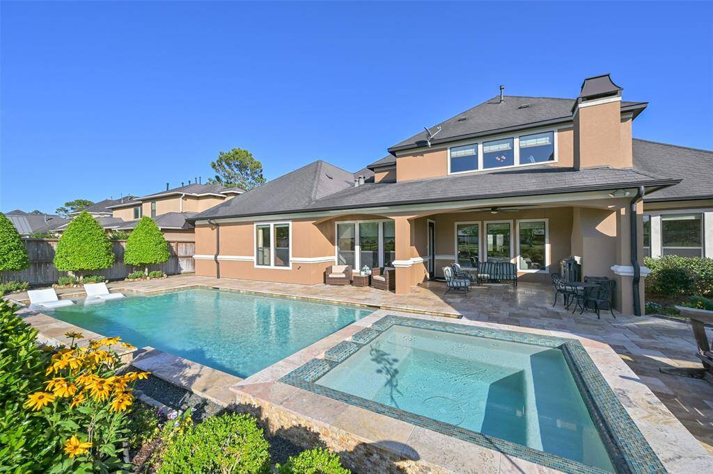 This photo showcases a spacious backyard with a modern pool and spa, surrounded by a well-maintained travertine patio and landscaping. The home features two covered outdoor patios, perfect for relaxation.