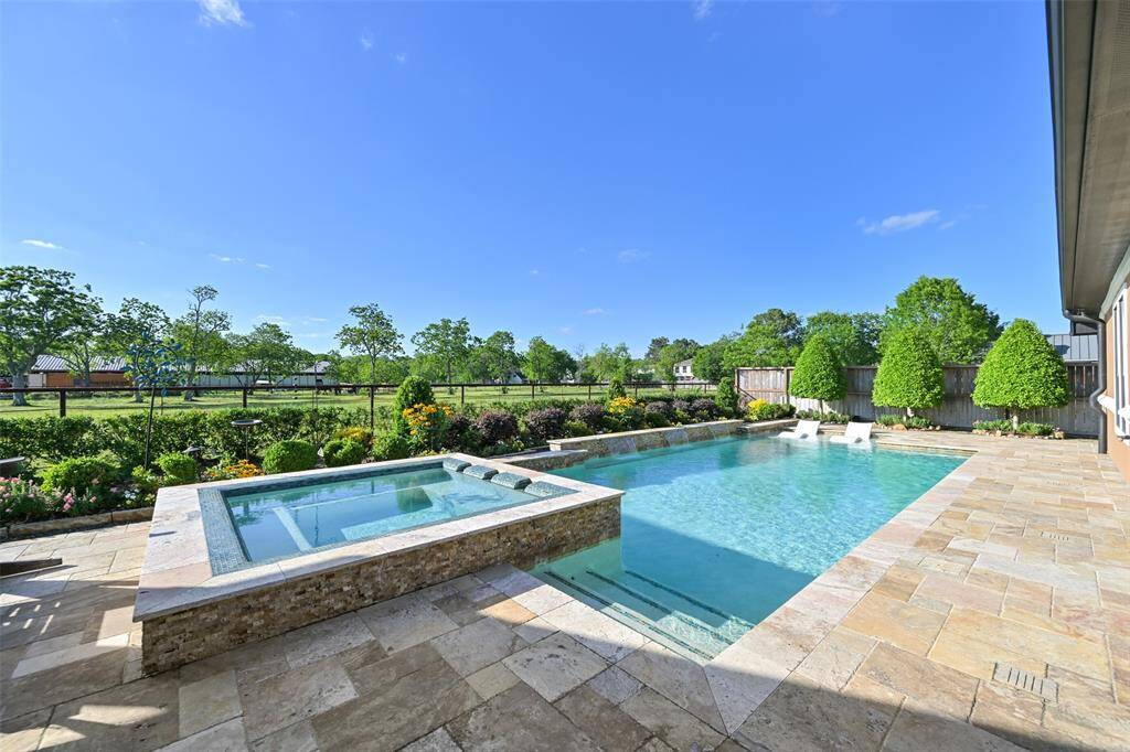 This photo showcases a luxurious backyard featuring a sparkling pool with waterfall fountains and oversized hot tub, surrounded by a landscaped garden with lush greenery and a view of quiet horse fields. Perfect for relaxation and outdoor enjoyment.