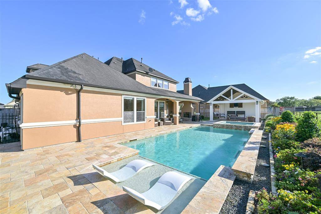 This photo showcases a spacious backyard featuring a luxurious pool with built-in lounge chairs and tanning deck.