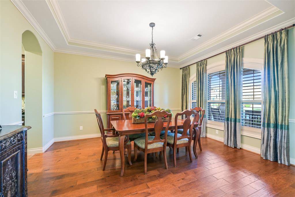 This elegant dining room features hardwood floors, stylish tray ceilings, and large windows with plantation shutters.