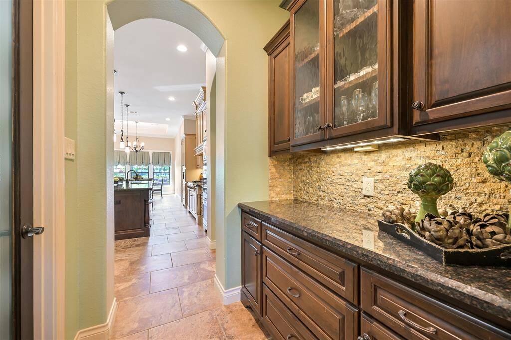The butler pantry showcases elegant dark wood cabinetry and beautiful glass display leading to a bright kitchen area and frosted glass pantry access.