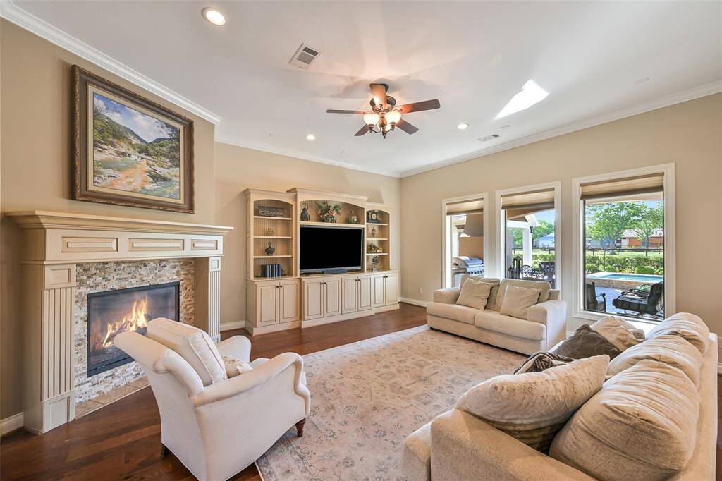 This spacious living room features an over-sized fireplace, 12' wide built-in shelving, and large windows offering ample natural light and views of the outdoor patio and neighboring horse pasture. Neutral tones and a ceiling fan add to the inviting atmosphere.