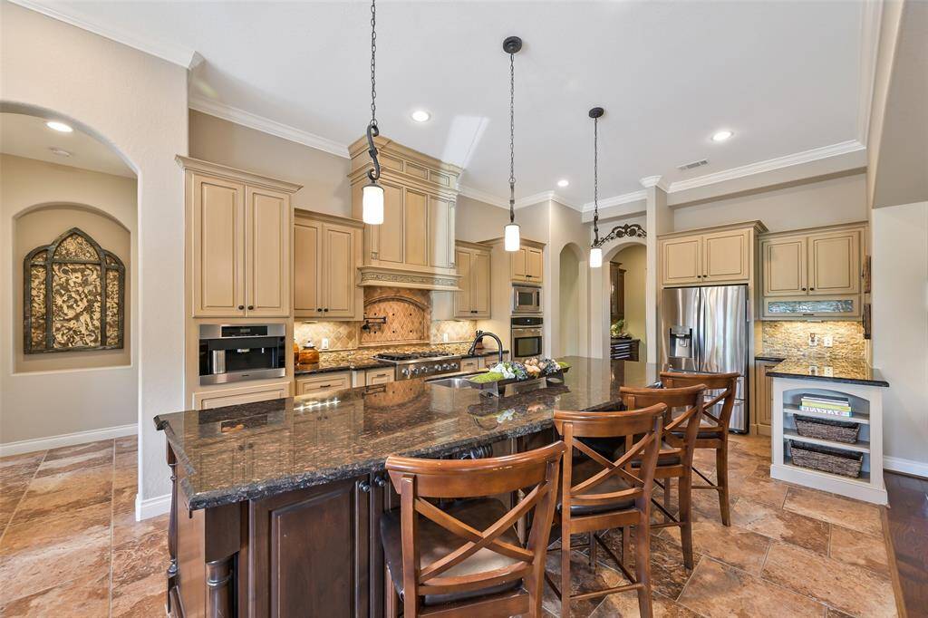 This kitchen features a 12' island with beveled edge granite countertops perfect for entertaining. It includes specialty stainless steel appliances, custom two-toned cabinetry, creating a warm and inviting space with ample storage and functionality.
