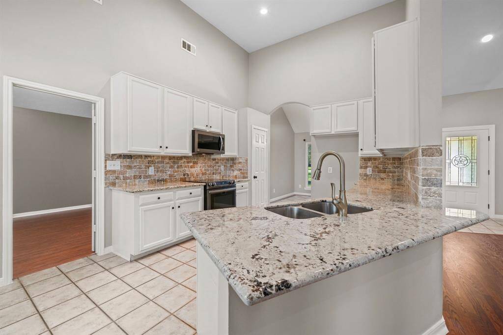 Bright kitchen featuring granite countertops, a double sink, and stainless-steel appliances. The space includes tile flooring and a stone backsplash, with an open layout leading to breakfast room and Livingroom.