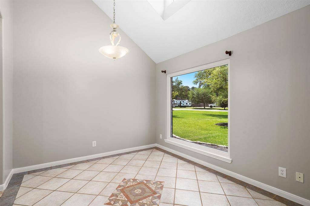 This room features a large window offering a scenic view of a green lawn and trees. It has neutral-colored walls, tiled flooring with a decorative center, and a modern hanging light fixture, creating a bright and inviting space.