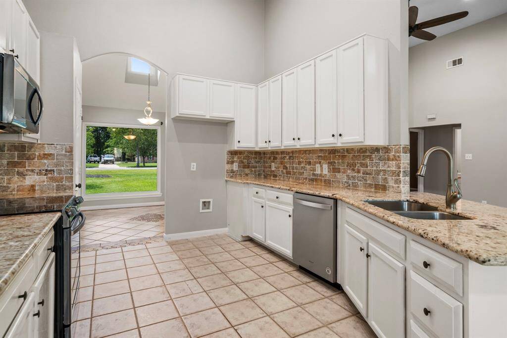 Spacious kitchen with high ceilings, featuring white cabinets, granite countertops, and a stone tile backsplash. Includes stainless steel appliances.