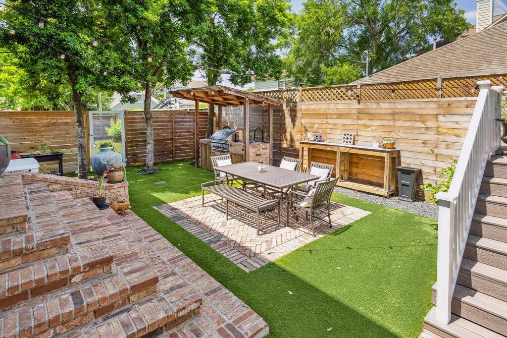 The brick-lined patio features a covered outdoor kitchen and al fresco dining area shaded by mature trees —perfect for entertaining.