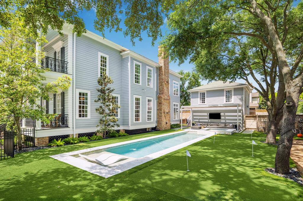 This view showcases the scale and beauty of the home's architecture, with a stunning blend of symmetry, large windows, and charming landscaping surrounding the pool area.